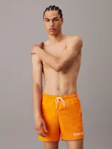 Bañador corto color naranja con cintura elástica ajustable con cordón blanco, bolsillos laterales y logo de Calvin Klein estampado en blanco en la pierna izquierda.