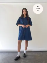 Vestido camisero corto de denim azul, con cuello camisero, mangas cortas y abotonadura frontal.
