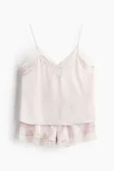 Conjunto de pijama color rosa pálido, de satén, compuesto por un top lencero con escote en V, breteles finos ajustables y ribetes de encaje, y un short con cintura elástica y ribetes de encaje.