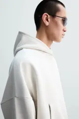 Sudadera con capucha color crudo, corte boxy, manga larga y bolsillo tipo canguro.