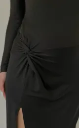 Vestido largo negro de mangas largas, con escote redondo y tajo lateral. Incluye cinturón de cuero negro con hebilla plateada y tachas.