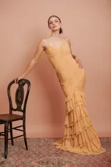 Vestido largo color durazno, entallado, con escote en V, breteles finos, drapeado en el frente y falda con volados.