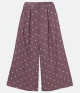 Pantalón pantacourt de viscosa color lila con estampado de pequeños cuadrados blancos. Tiene pinzas delanteras, bolsillos laterales y cierre con botones.