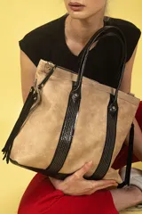 Bolso tipo tote de cuero graneado color beige con detalles en cuero negro brillante. Tiene doble asa corta, correa larga regulable y flecos laterales. Interior forrado con bolsillo con cierre y bolsillo para celular.