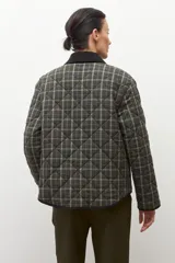 Campera capitoneada con diseño acolchado y estampado a cuadros en tonos verde oliva. Presenta un cuello de pana en color negro, cierre frontal de botones y bolsillos delanteros con ribetes oscuros.