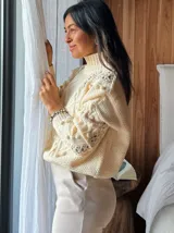 Sweater tejido grueso color rosa, con cuello alto, mangas largas y diseño trenzado con detalles de pompones.
