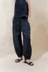 Pantalón de lino a rayas verticales azul marino y blanco, con corte amplio, tiro medio, pretina ancha con doble abotonadura, bolsillos laterales, pinzas en el frente y ruedo con presilla para usarlo recto o fruncido al tobillo.
