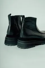 Bota corta de cuero negro, estilo botín chelsea, con puntera cuadrada y suela track gruesa y robusta.