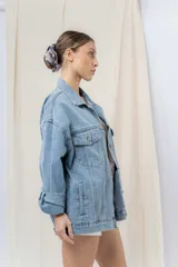 Campera denim celeste de corte oversize, con cuello clásico, cierre frontal con botones metálicos, bolsillos delanteros con solapa, bolsillos laterales y mangas largas con puños abotonados.