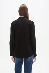 Camisa de viscosa color crema con finas rayas verticales negras, corte al cuerpo, cuello camisa y dos bolsillos frontales con tapa. Posee botones frontales y mangas largas con puño.