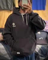 Canguro oversized color gris oscuro con capucha y estampado en la espalda que dice "TRIBU BRAND" y "THE JOURNEY CONTINUES SUMMER VOLUME II" junto a dos soles.