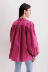 Camisa fucsia de algodón, corte holgado, con cuello camisero, cierre frontal con botones y mangas largas abullonadas con puños abotonados.
