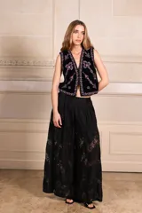 Chaleco color beige con bordados florales en tonos violeta y rosa, sin mangas y con cierre frontal con ganchos.