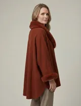 Ruana tejida color terracota, de corte amplio y asimétrico, con cuello y puños adornados con apliques de piel sintética del mismo tono.
