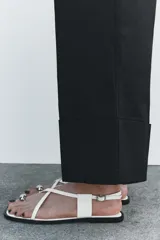 Pantalón color beige de corte ancho, con tiro medio, trabillas en la cintura y raya planchada.