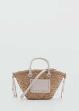 Bolso tipo canasta de paja color beige con aplique rectangular de cuero sintético blanco con tachas doradas. Tiene doble asa de mano y correa larga desmontable.