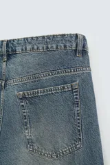 Pantalón de denim color beige, corte relaxed fit, con bolsillos laterales tipo cargo con solapa y cierre de botón. Cierre frontal con botón y cremallera.