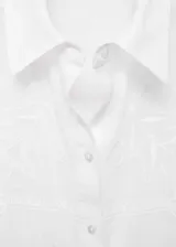 Camisa blanca de algodón con bordados florales, de corte oversize, manga larga con puños abotonados y cuello camisero.