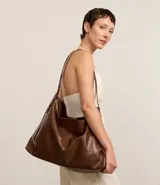 Cartera hobo grande de material sintético color marrón, con cierre de botón a presión y asa larga con detalle de eslabones metálicos.