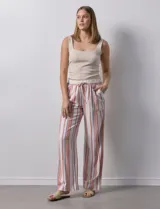 Pantalón de lino color blanco con rayas verticales rosas y celestes. Tiene pretina ancha elastizada con lazo de ajuste y bolsillos inclinados en la parte delantera.