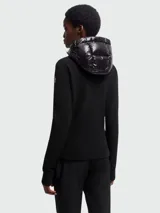 Chaqueta híbrida negra de Moncler, con cuerpo acolchado brillante y mangas de tejido de punto liso. Cuenta con capucha ajustable y cierre frontal de cremallera.