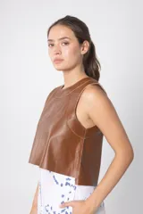 Chaleco corto marrón de cuero con cuello redondo y costuras a la vista.