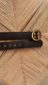 Cinturón negro de cuero con hebilla circular dorada.