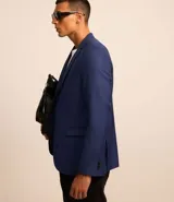 Saco de traje azul cobalto, modelo social, con cuello solapa, abotonado delantero, bolsillos y mangas largas.