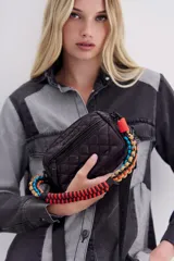 Bandolera negra de nylon matelassé con correa larga regulable y correa corta desmontable de cordones trenzados multicolores. Tiene cierre superior, bolsillo frontal con cierre, bolsillo trasero y dos bolsillos internos.