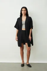 Camisa negra de manga corta, estilo kimono o bata ligera, con cuello solapa y bolsillos frontales amplios.