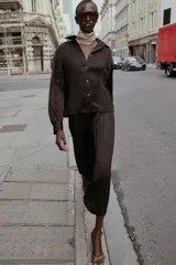 Camisa oversize color marrón oscuro confeccionada en tejido satinado con efecto arrugado, cuello solapa, manga larga con puños y cierre frontal con botones metálicos.