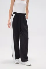 Pantalón de jogging negro con cintura elástica, corte holgado y una franja vertical blanca a lo largo de la pierna.