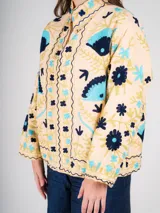 Chaqueta color crema con bordados de flores y figuras geométricas en tonos azul, celeste y dorado.