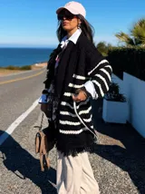 Sacón negro con rayas horizontales blancas, tejido tipo mohair, corte oversize y cinturón ajustable.