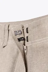 Pantalón de tiro bajo color beige, con bolsillos delanteros y falsos bolsillos de vivo en la espalda. Piernas rectas y cierre frontal con cremallera, botón interior y ganchos.