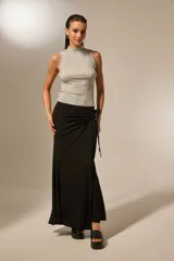 Falda larga negra con detalle de nudo lateral y tiras colgantes, de corte ajustado en la parte superior y ligeramente acampanado en el ruedo.