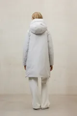 Campera acolchada larga, color blanco, con capucha grande y cierre frontal de cremallera negra. Presenta bolsillos laterales con cremallera negra.