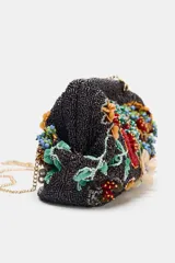 Bolso de mano con cuerpo en abalorios negros y diseño floral multicolor. Tiene asa de anillas metálicas extraíble en forma de bandolera, bolsillo interior y forro interior. Cierre mediante clip.