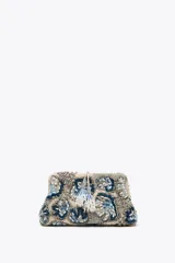 Bolso de mano tipo clutch con cuerpo cubierto de abalorios en tonos beige, azul y gris. Tiene un diseño floral y un cierre imantado. Incluye correa metálica extraíble y bolsillo interior con cremallera.