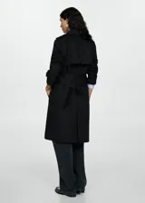 Trench coat negro con cuello de solapa, doble botonadura, trabillas en los puños, cinturón ajustable y abertura posterior en el bajo.