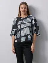 Blusa de gasa estampada con flores verdes sobre fondo blanco, de la marca Sioni. Tiene mangas cortas amplias con abertura y botón.