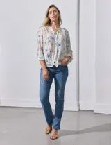 Blusa de gasa estampada con rayas verticales en tonos naranja, amarillo y blanco. Tiene cuello a la base, escote en V y botones. Delantera con bolsillo aplicado. Largo de manga regulable con presilla y botón. Terminación anudada opcional.