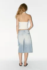 Camiseta blanca de rib con efecto lavado, cuello halter y escote redondo. Detalle de arandelas metálicas en el escote.