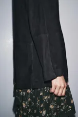 Chaqueta de ante negra con cuello solapa de muescas y manga larga. Tiene bolsillos con solapa en delantero y cierre frontal con botones.