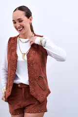 Chaleco marrón de gamuza sintética con apliques de flores y tachas doradas.