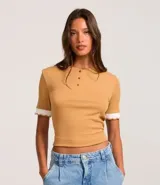 Blusa de manga corta color ocre, confeccionada en tejido rib con viscosa certificada. Tiene cuello redondo, botones delanteros y detalle de retilínea contrastante en el bajo de las mangas.