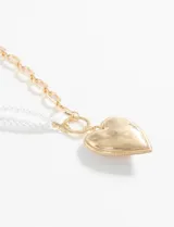 Collar con cadena de eslabones dorados y dije en forma de corazón, combinando perlas blancas.