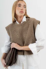 Chaleco de lana color crema, tejido a punto perlado con calado en la parte delantera. Tiene cuello a la base y silueta cuadrada.