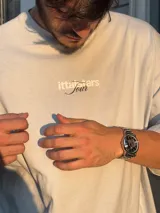 Remera rosa de corte recto con estampado en la espalda que incluye el texto "Itta Tours", "Tour", y nombres de ciudades como Ibiza, Madrid, Andorra, Barcelona y Formentera.