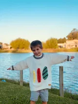 Sweater de lana color crema con cuello redondo y mangas largas. Presenta tres tablas de surf bordadas a mano en amarillo, rojo y turquesa.